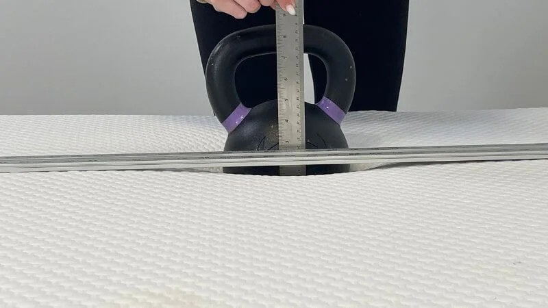 Our tester rating the sinkage exhibited on the Nolah Original mattress with a ruler and kettlebell