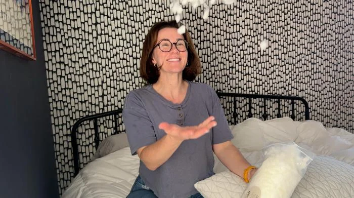 A person smiles while tossing filling in the air from a Coop Sleep Goods Original Adjustable Pillow