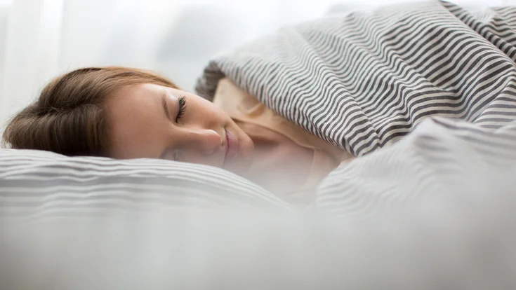 A woman sleeps under striped covers.