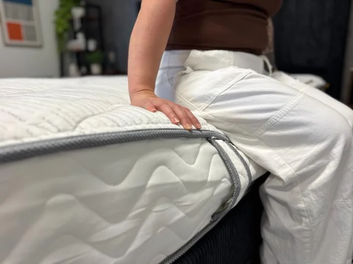 A woman sitting on the edge of the DLX Classic Two-Sided Mattress