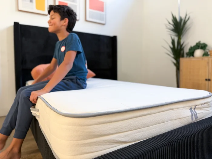 A young tester sits on the edge of the Nolah Nurture mattress to judge its support