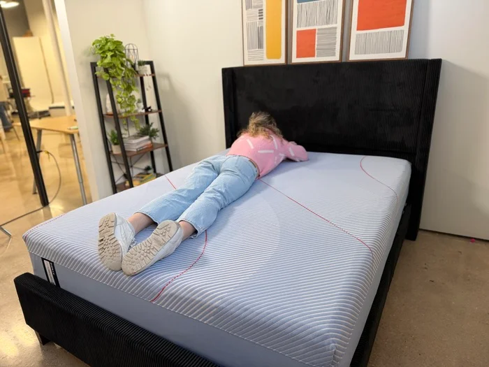 woman in a pink sweater resting on her stomach on a sealy posturepedic hybrid mattress