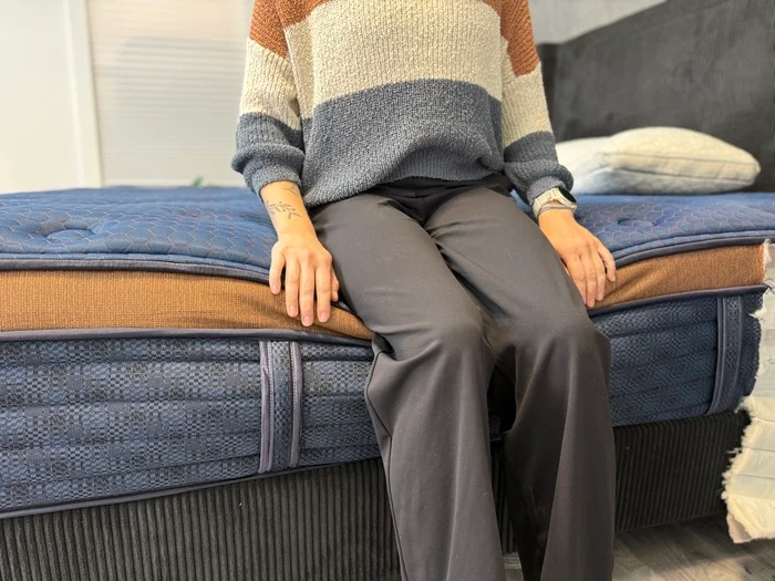 A woman seated on the edge of the Aurora Luxe mattress