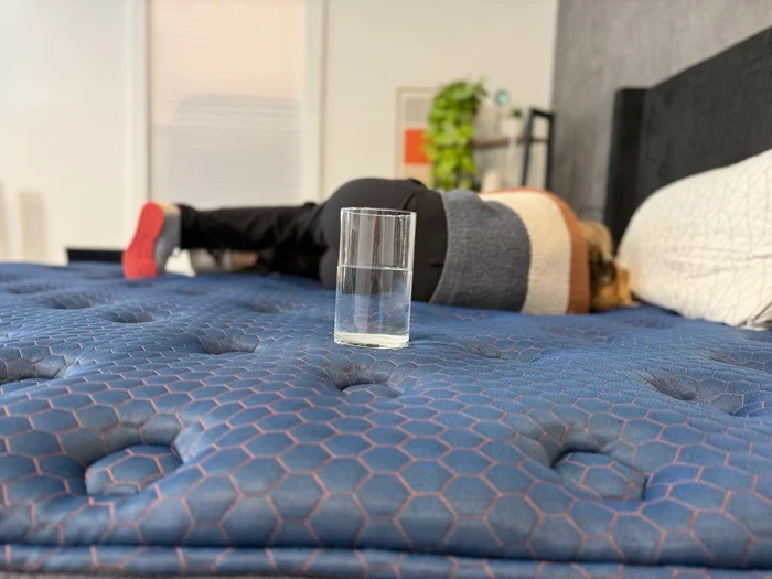 A water glass perched on the surface of the Aurora Luxe Cooling while a tester rests on the other side