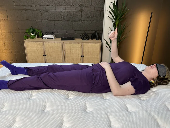 A woman wearing a sleep mask gives the thumbs-up to indicate felt movement on the Brooklyn Bedding Signature Hybrid mattress