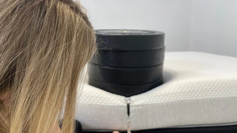 Our tester measuring perimeter sinkage on the Nolah Original mattress with a stack of bumper plates and measuring tape
