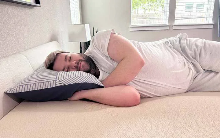 A man rests on his side on top of the Plushbeds Latex topper.
