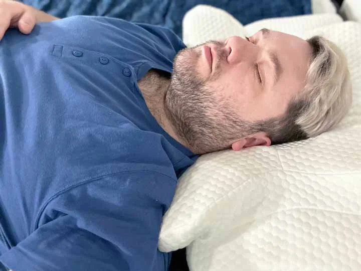 A man sleeps on his back while resting on the Zamat Butterfly Cervical Pillow. A man sleeps on his back while resting on the Zamat Butterfly Cervical Pillow.