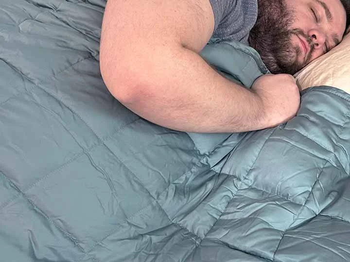 A man sleeps while using the YnM weighted blanket.