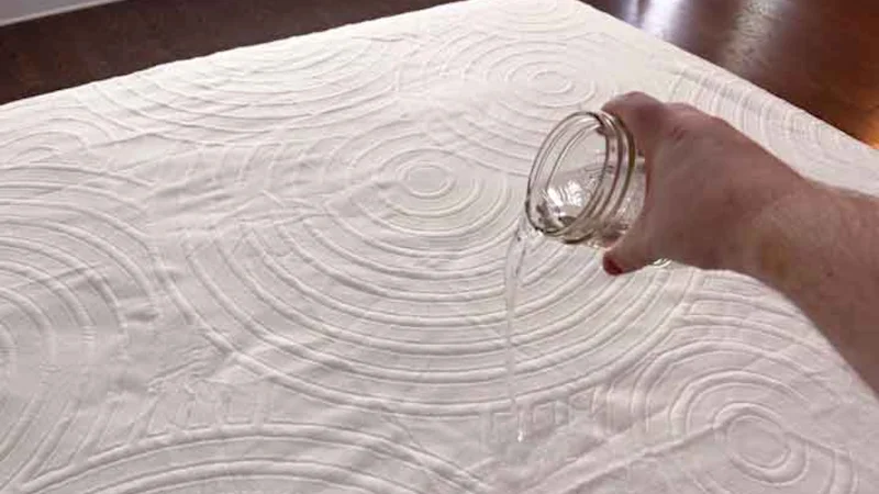 An image of a hand pouring water on top of the TEMPUR-Protect Mattress cover to show its waterproofing.