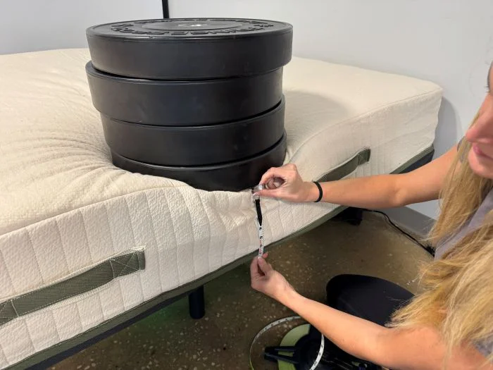 A woman measures sinkage with 4 weights on the Avocado Eco Organic Mattress