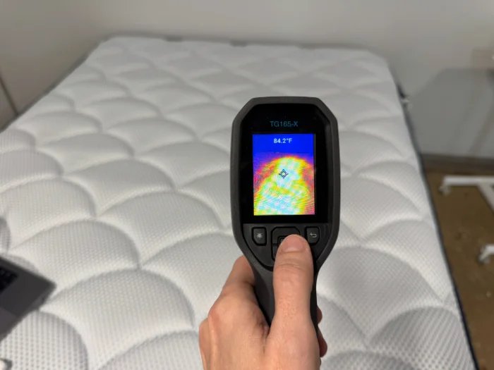 A temperature gun with a reading of 84.2 degrees Fahrenheit pointed at the DreamCloud Premier mattress