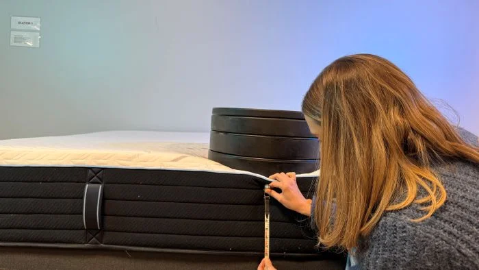 A woman places weights on the Nectar Classic Hybrid mattress to measure sinkage.
