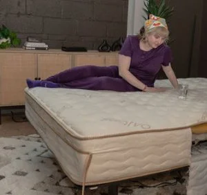 A woman testing motion isolation by jostling the Saatva Classic while a glass of water is balanced on its surface