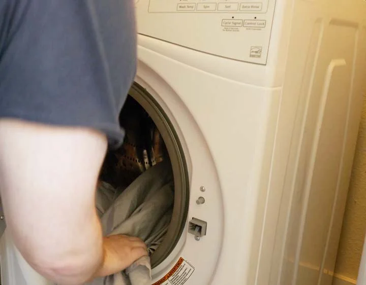 GhostBed Sheets - a man loads the sheets into a washing machine. man loads the GhostBed sheets into a washing machine