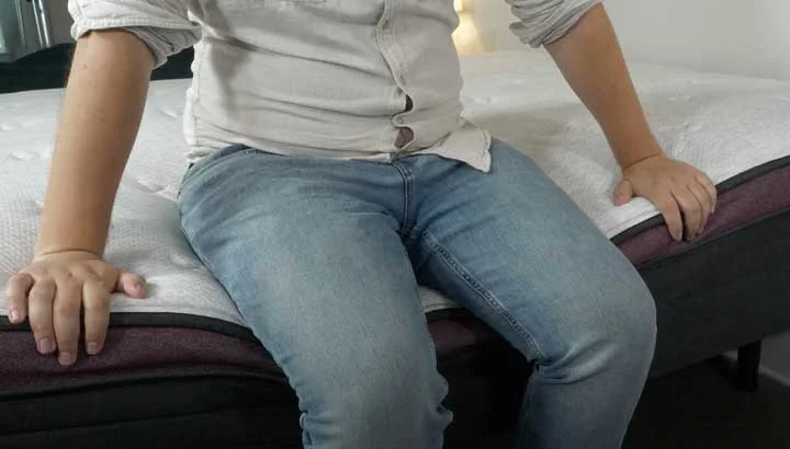 A man sits on the edge of the Helix Dusk Luxe mattress