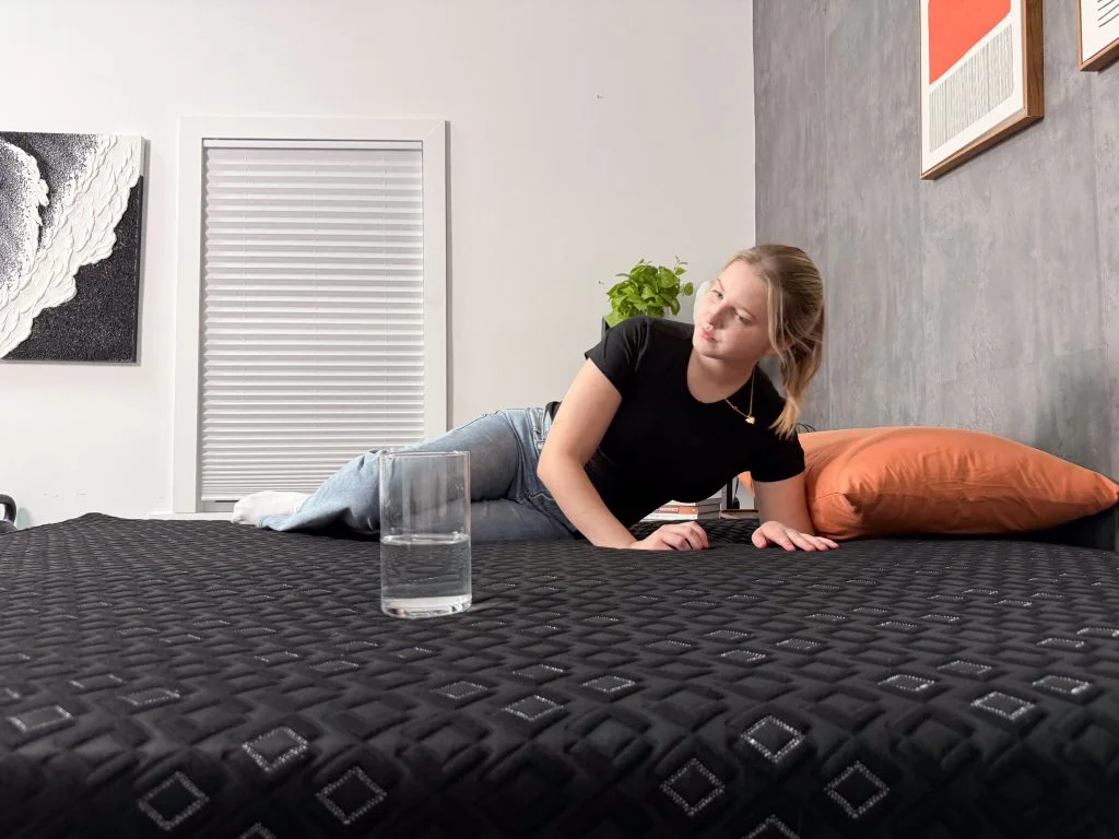 A glass of water sits on one side of the Beautyrest Black Hybrid XCS while our tester moves around on the other