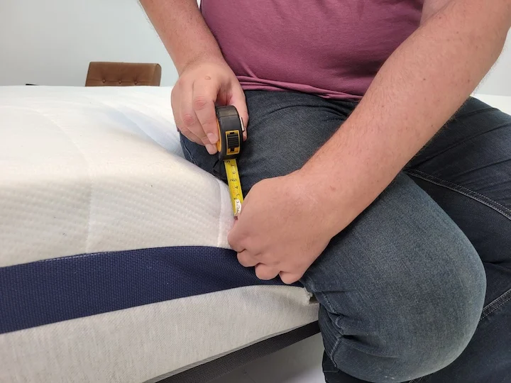 A man sits along the side of the Helix Midnight mattress and measures its sinkage