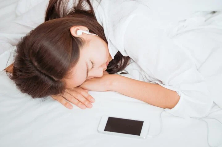 a woman sleeps next to her phone with airpods in her ear