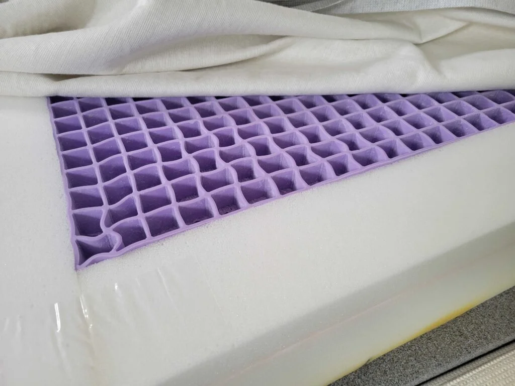 The cover of the Purple NewDay mattress is lifted to show the surrounding support foam and center Purple gel grid.