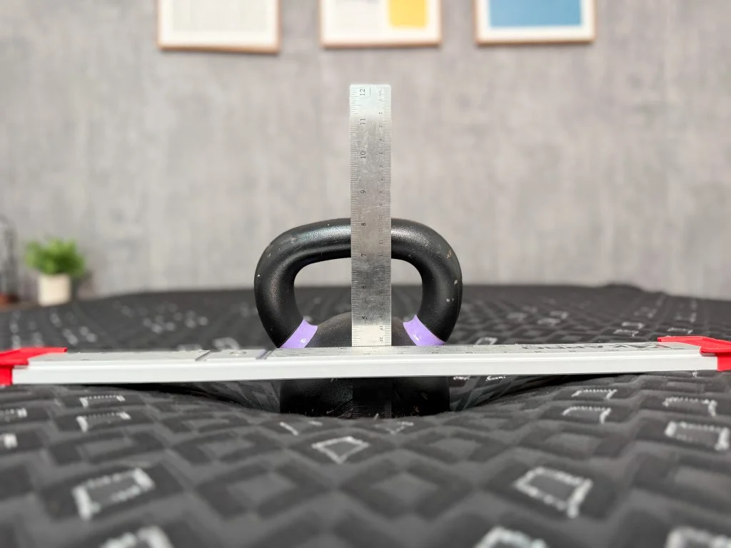 A kettlebell resting on the surface of the mattress while a ruler measures the sinkage depth