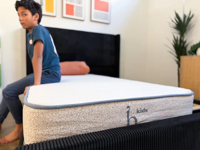 A young tester sits on the edge of the Birch Kids mattress to judge its support