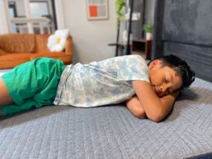 A young boy in a blue shirt and green shorts rests on his side on the Brooklyn Bedding Kids mattress