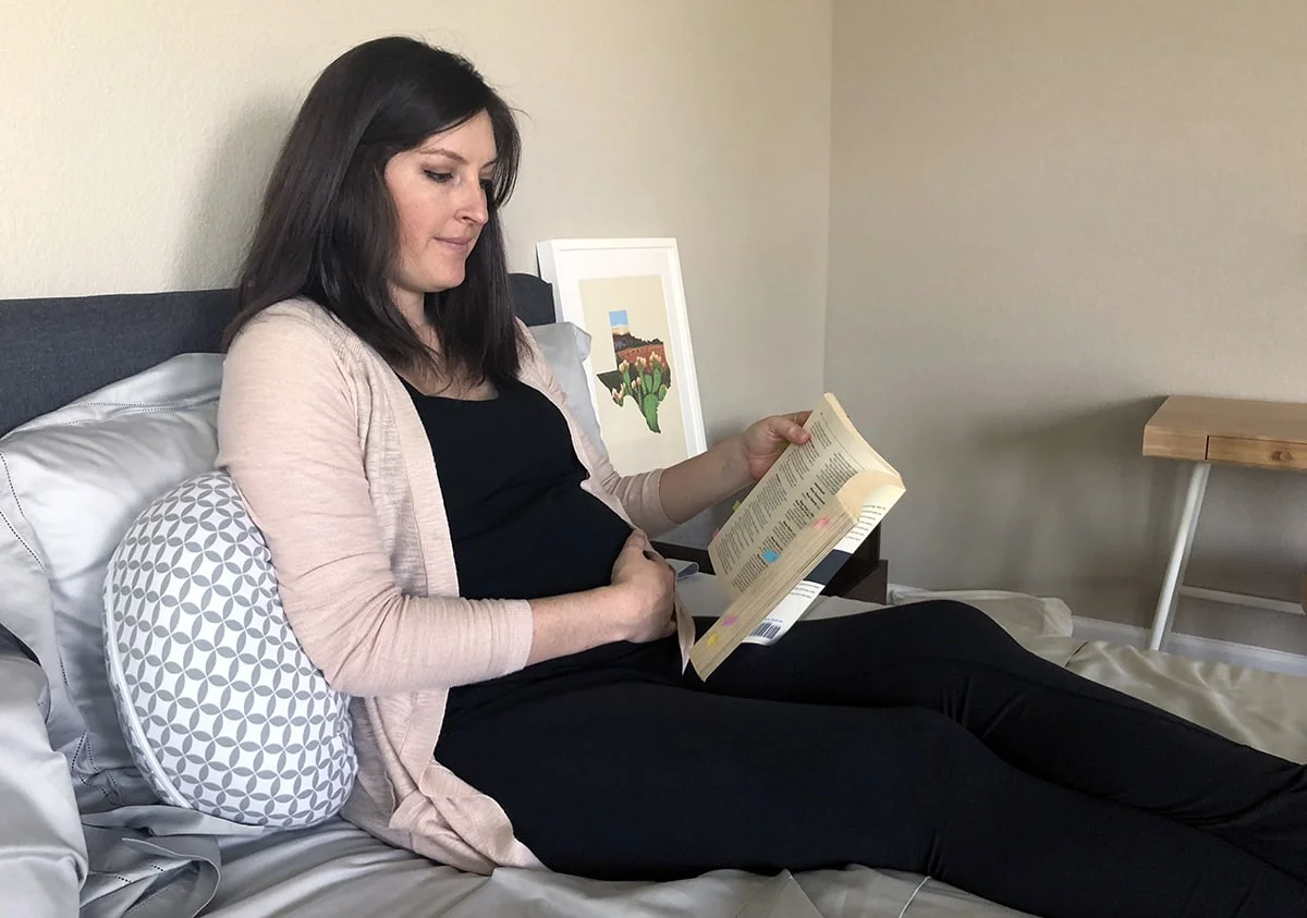 a woman uses the boppy side sleeper pillow as an arm rest, while she reads a book in bed a woman uses the boppy side sleeper pillow as an arm rest, while she reads a book in bed