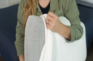 A woman pulls the white cover off the Tuft & Needle Original Foam pillow to show the foam core. A woman pulls the white cover off the Tuft & Needle Original Foam pillow to show the foam core.