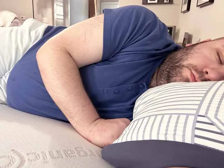 A man sleeps on his side while on top of the Titanflex Mattress Topper