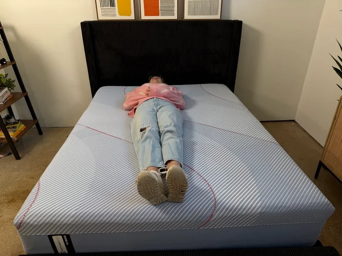 woman in a pink sweater resting on her back on a sealy posturepedic hybrid mattress