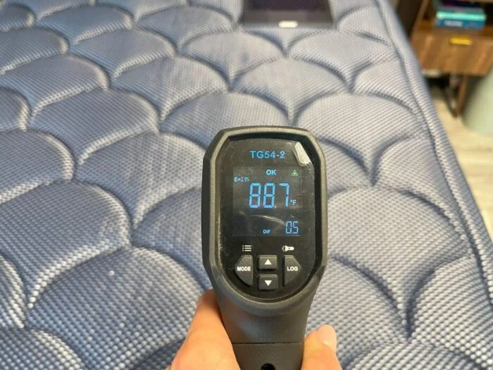 Our tester using a temperature gun to measure the DreamCloud Luxe Memory Foam mattress after laying down