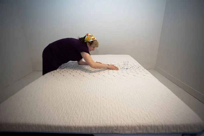 A woman tests motion isolation with a glass of water on the Nectar Classic Hybrid mattress.