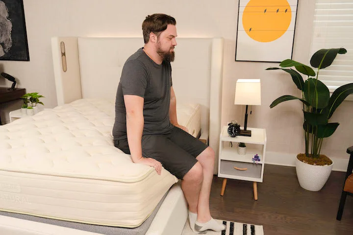 A man sits on the edge of the Bear Natural mattress