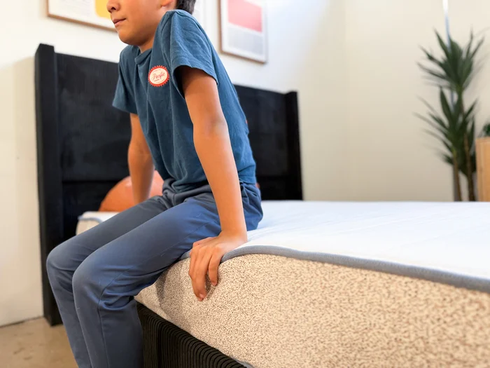 A young tester sits on the edge of the Birch Kids mattress to judge its support