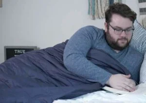 A man lounges with the Sleep Number True Temp weighted blanket while reading a book.