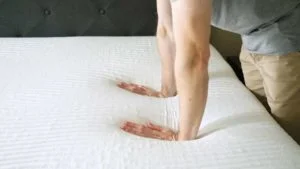 Two hands pushing down firmly on a mattress.