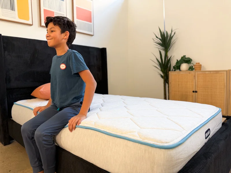 A young boy sits on the edge of the Bear Cub mattress