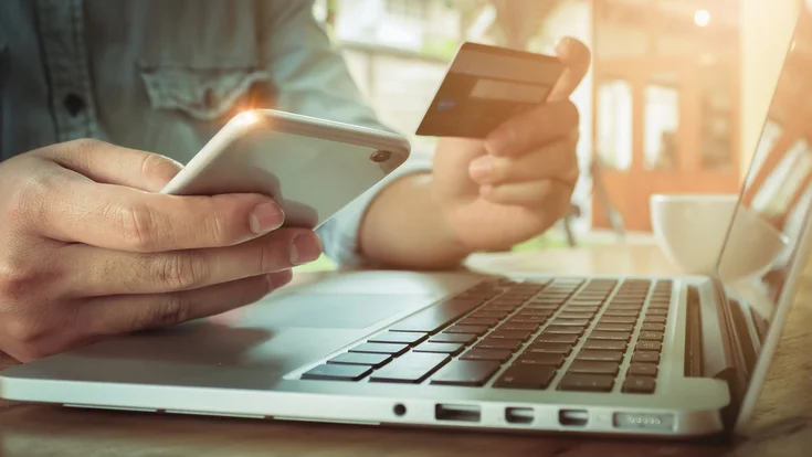 A man holds his credit card and smart phone, preparing to order online.