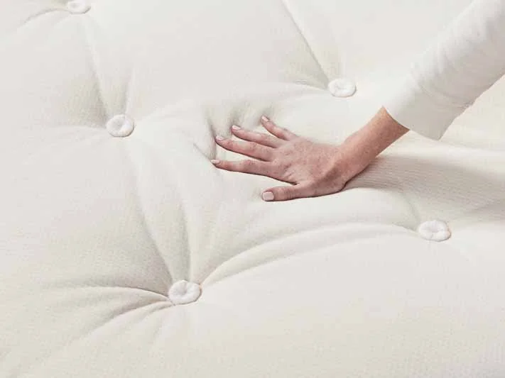 A woman places her hand on a mattress.