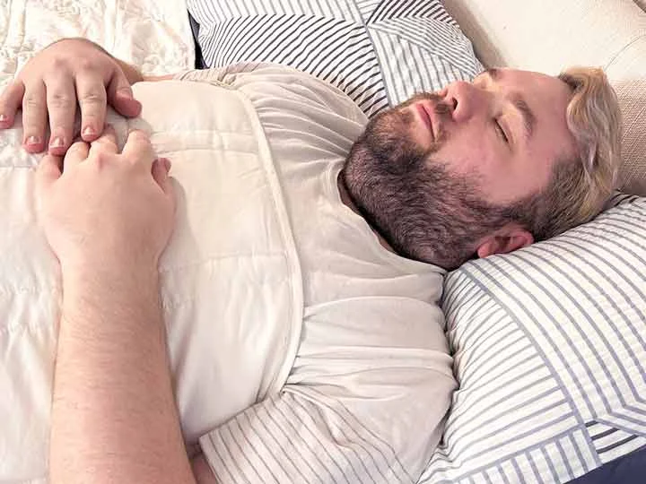 A man sleeps on his back while using the Baloo weighted blanket.