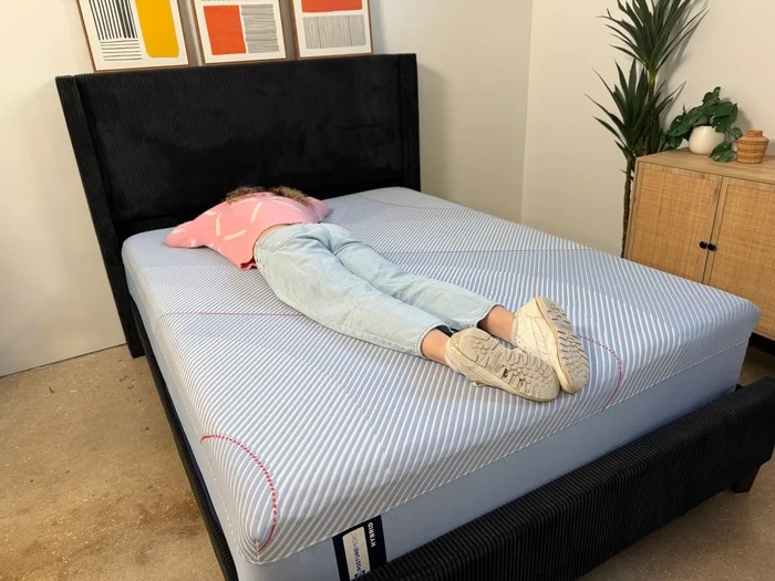 woman in a pink sweater resting on her stomach on a sealy posturepedic hybrid mattress