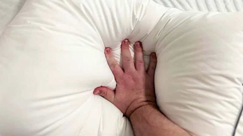 A hand pressing firmly into a down pillow