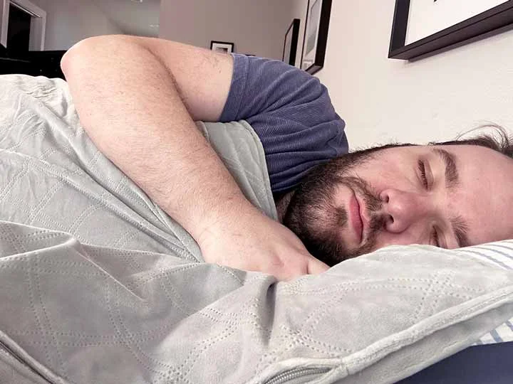 A man sleeps with the Puffy weighted blanket over him.