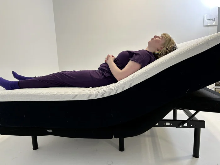 A woman lies on the Nectar Classic mattress with its head elevated by an adjustable base
