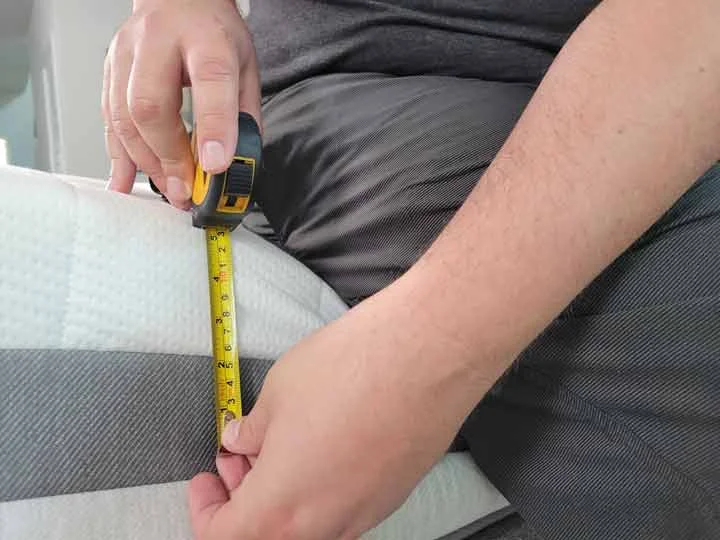 A close up image of a man sitting on the edge of the Helix Plus mattress. He has a tape measure to show the sinkage of the edge.