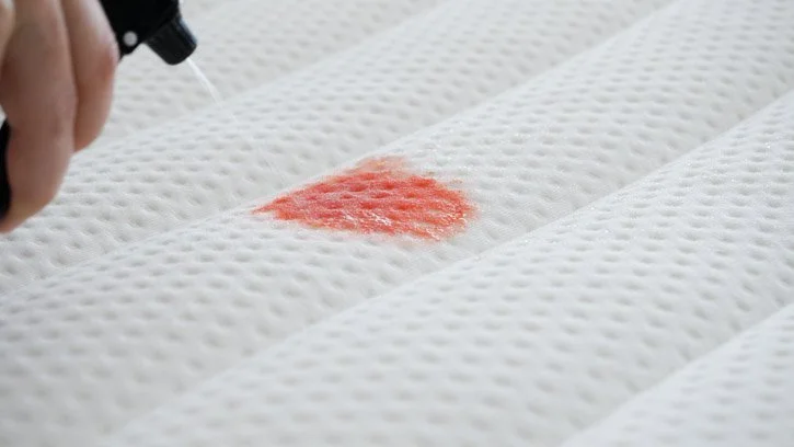 A person cleans a blood stain from a mattress A person cleans a blood stain from a mattress