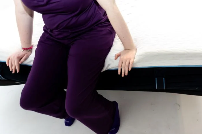 A woman sits on the edge of the Nectar Classic Hybrid mattress.