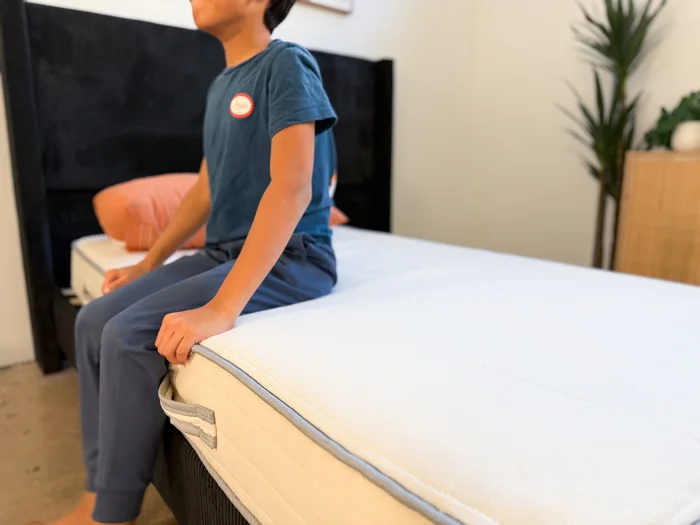 A young tester sits on the edge of the Nolah Nurture mattress to judge its support