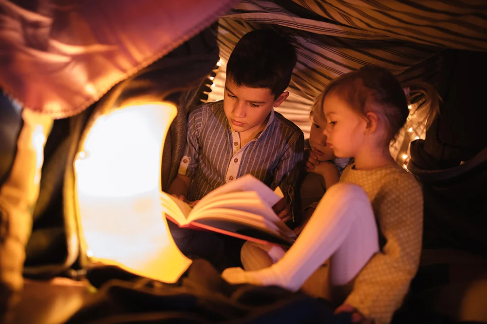 Brother reading a story to his younger siblings in a fort at night Brother reading a story to his younger siblings in a fort at night
